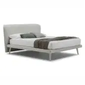 Beige upholstered bed with rectangular headboard, conical legs, and light beige fabric, styled with white and gray pillows and a gray throw blanket.