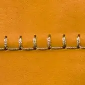 Yellow leather texture displaying horizontal looped stitching with light-colored thread, exhibiting a smooth, tactile surface and warm golden hue.