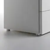 White cabinet with brushed aluminum cylindrical feet and two drawers on a light gray floor, minimalist design.