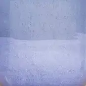 Pale blue granular powder in clear glass vessel, textured surface, consistent hue, diffused lighting, granular accumulation.