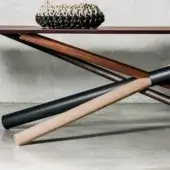 Wooden dining table with dark brown top and three-tone cylindrical legs, featuring beige woven bowl on light gray concrete backdrop.