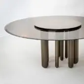 Bronze glass table with oval tabletop and four tapered, light bronze cylindrical legs on a smooth, light floor.
