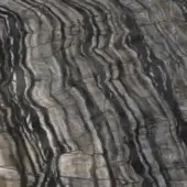 Sedimentary rock texture displaying undulating gray and beige bands, with fractures and angular blocks forming a rough, layered surface.