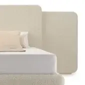 Bed with boucle headboard and platform, off-white fabric, rounded shape, gold trim, white cotton linens, studio shot.