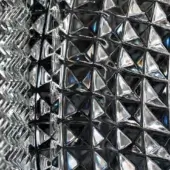 Crystal sculpture “alba” with geometric carved facets, displaying iridescent blue and silver highlights from refracted light.