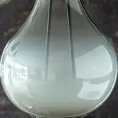 Glass vase, pearlescent white, rounded shape with internal gray lines, displayed on dark polished stone surface with blurred background reflection.