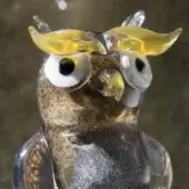 Glass owl sculpture, clear with amber swirls, featuring white eyes and yellow ears, studio backdrop.