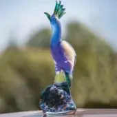 Glass peacock figurine, deep blue and gold, sculpted with raised head and swirling tail feathers on a clear glass base.