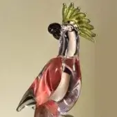 Glass parrot sculpture, clear with red accents, stylized wings down, black head, and green crest against a beige backdrop.