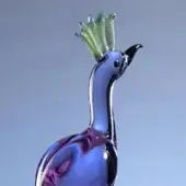 Glass peacock sculpture, translucent purple and blue, with curved neck and green feather crest against a gradient blue backdrop.