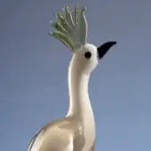 Glass bird sculpture, translucent white with gold shimmer, featuring layered golden and pale green feather crest and sharply pointed black beak.