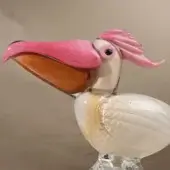 Glass pelican sculpture, white and gold, with pink beak and crest, mounted on a clear glass base, glossy finish.