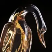 Blown glass duck sculpture, amber and clear, stylized form with elongated body and curved neck, reflective surface, black background.