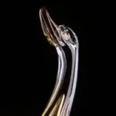 Glass duck sculpture, amber-colored beak, upward-facing pose, transparent body, smooth finish, black background, focused lighting, art object.