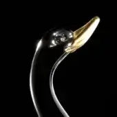 Sculptural duck head, dark gray metal, upward curving gold beak, reflective surface, black background, focused studio lighting.
