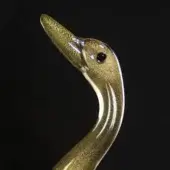 Glass duck sculpture, mottled gold and grey, upward-facing pose with etched neck details and dark bead eye against black backdrop.