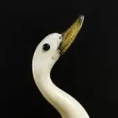 Glass duck sculpture, creamy white and gold, with curved neck and tilted head, featuring a dark blue glass eye and textured beak.