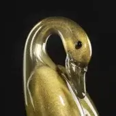 Glass swan sculpture, gold speckled finish, curved neck profile, black eye, reflective surface, smooth contours, dark background.