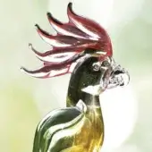 Glass parrot sculpture, green and yellow blown glass, with pink crest and clear beak, displayed in profile against a light green backdrop.