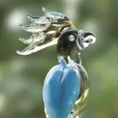 Glass parrot sculpture, blue and amber, dynamic pose with detailed translucent wings, mounted on clear rod, blurred green background.