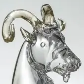 Glass ram sculpture, transparent with gold horns, detailed head and neck, frosted texture, soft lighting, against a light gray backdrop.