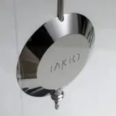 Chrome Takto pendulum showerhead features a circular lens with vertical striations and etched brand name against a white wall.