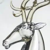 Glass deer sculpture with gold antlers, detailed facial features, and a transparent elongated base, displayed against a light wall.