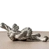 Sculptural object, silver-toned metal, tangled organic form with textured surface and reflective finish on a light wood background.