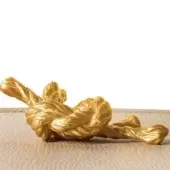 Sculptural gold form, polished 24k gold finish, twisted knot design on light wood surface against a white backdrop.