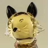 Glass cat sculpture, champagne-colored, with black ears and collar, featuring etched whiskers and asymmetrical dark eyes, smooth rounded form.
