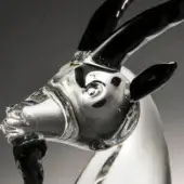 Glass goat head sculpture, clear and black, elongated snout with swirling patterns, detailed eyes, glossy horns against a gray backdrop.