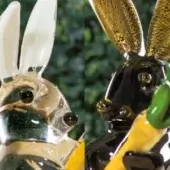 Rabbit figurines, transparent & black, with amber inclusions, gold accents, elongated ears, and stylized design against green foliage.