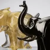 Glass elephant figurines, transparent and black, with gold flecks and smoky gray tints, showcase modern stylized design and reflective surfaces.