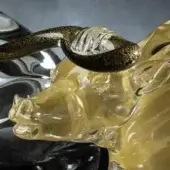 Glass ox head sculpture, amber tone, with black and gold segmented horn; reflective silver backdrop.