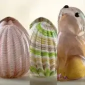 Glass seashell and rabbit sculptures, pink, gold, green, and white, displayed against a beige backdrop with translucent textures.