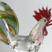 Glass rooster sculpture, transparent with red enamel head, pink and green detailing, swirling green, gray, pink tail feathers, studio lighting.
