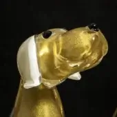 Glass dog sculpture, amber and gold, with white head and bone, black details, tilted pose, translucent texture, black background.