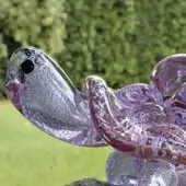 Glass tortoise sculpture, iridescent purple and silver, detailed shell with textured finish, dark eye, pink mouth, on a dark base.