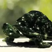 Green tortoise sculpture, dark jade stone, polished finish, detailed shell texture, walking pose, displayed on light wood surface.