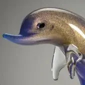 Glass dolphin sculpture with swirling blue and gold patterns, poised on a transparent sphere, studio lighting, gray background.