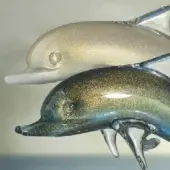 Glass dolphin figurines, white and aquamarine with gold shimmer, leaping pose on clear glass wave base, product shot.