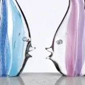Glass fish sculptures, blue & purple striped, clear glass with exaggerated eyes and open mouths on reflective gray surface.