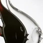 Glass sculpture, red and transparent, depicting two intertwined stylized fish with curved bodies and a sleek, elongated form.