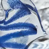 Glass clownfish sculpture with transparent form, featuring swirling blue glass streaks, elongated fins, and a glossy, reflective finish.