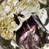 Glass sculpture, transparent with gold flecks, featuring a purple swirling center and curved glass tentacle mimicking a jellyfish form.