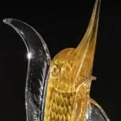 Glass marlin sculpture, amber and clear, with textured scales and curved fin, displayed against a black backdrop.
