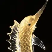 Gold glass marlin sculpture with translucent texture, angled upwards displaying detailed fins and a sleek, stylized body against black.