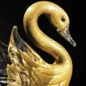 Glass swan sculpture, gold-colored finish, textured feathers, curved neck, clear beak, layered wings, reflective surface, black background.