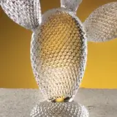 Glass sculpture, clear cactus ficus with flowers, textured squares, golden-yellow center, rounded form, concrete surface, yellow background.