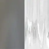 Translucent curtain with vertical folds and ridges, reflecting light against a solid grey wall, displaying draped texture and diffused lighting.